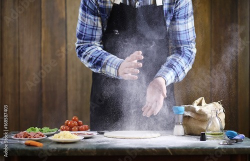 man preparing a pizza, knead the dough and puts ingredients