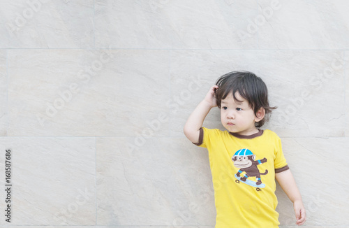 Closeup cute asian kid look at the space with confuse motion on marble stone wall textured background
