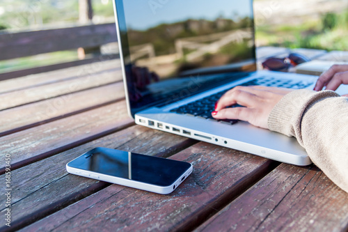 Woman working on a park on her laptop with black screen on a wood table.