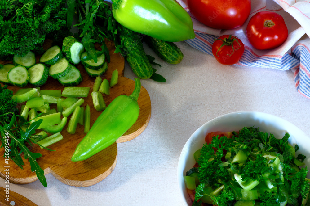 salad from pepper, parsley, tomato and cucumber in a white bowl on white wooden table salad from pepper, parsley, tomato and cucumber in a white bowl on white wooden table