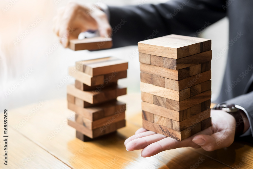 Planning, risk and wealth strategy in business concept, businessman and insurance gambling placing wooden block on a tower. Planning, risk and wealth strategy in business concept, businessman and insurance gambling placing wooden block on a tower.