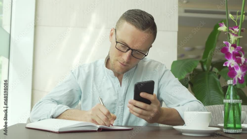 Businessman writing in daily planner and check notes on smartphone Businessman writing in daily planner and check notes on smartphone