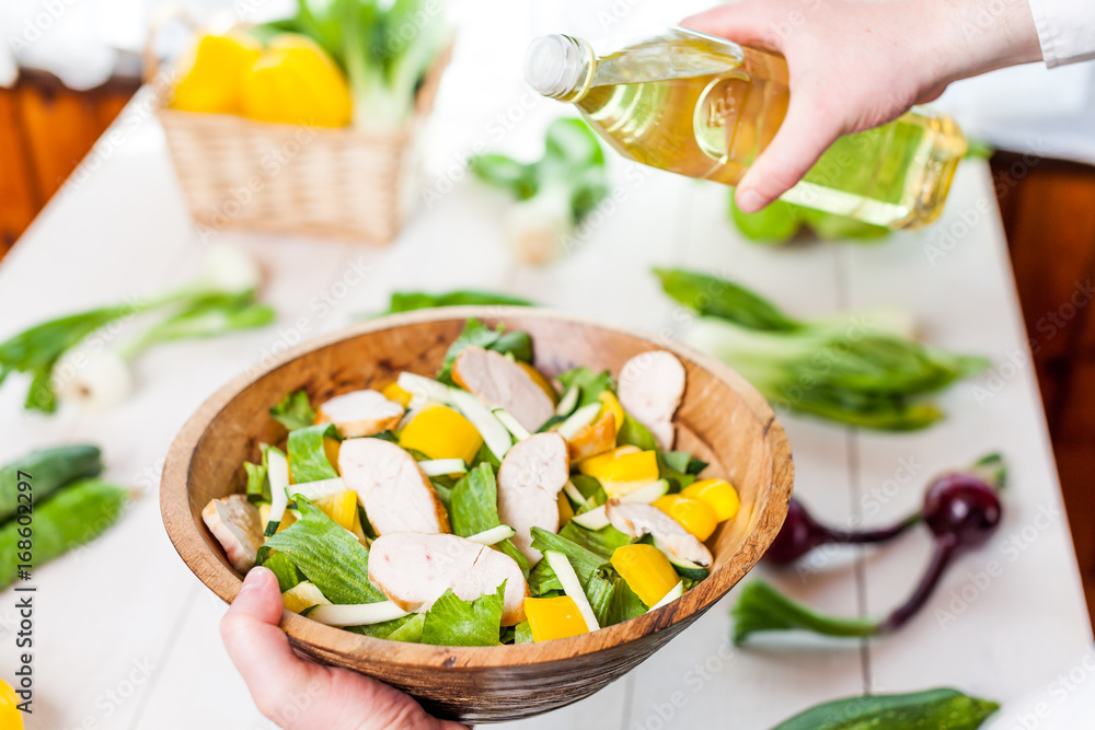 man pouring olive oil into healthy chicken salad on kitchen