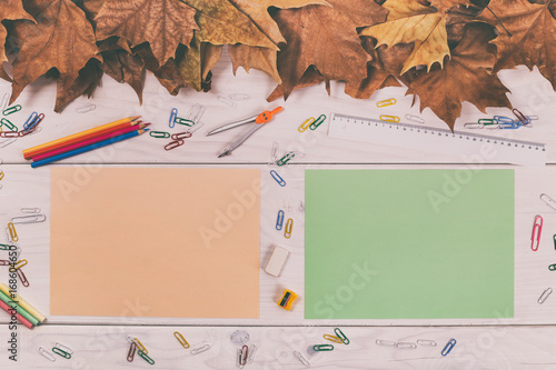 Empty colored papers and school supplies on wooden table with autumn leaves.