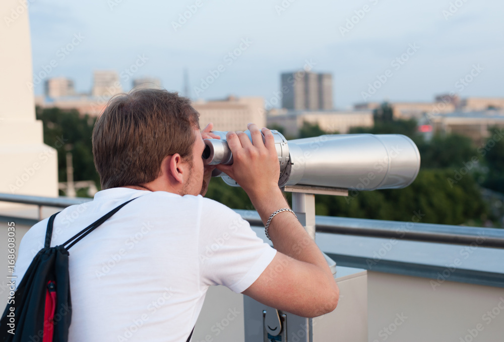 The young man looks at the tourist binoculars for sightseeing.
