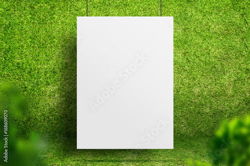 Blank white poster hanging at green grass room with blur leaf foreground,Ecology sustainable concept,Mock up for display of design