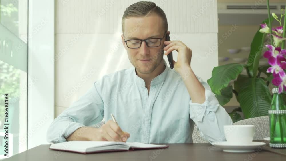 Businessman writing notes in personal organizer while talking on mobile phone with client. Businessman writing notes in personal organizer while talking on mobile phone with client.