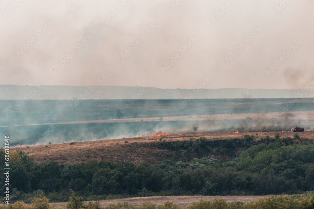 Burning grass in the fields and smoke from the fire rises, natural summer fires