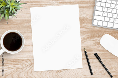 Blank a4 paper is in the middle of wood office desk table with supplies. Top view with copy space, flat lay.