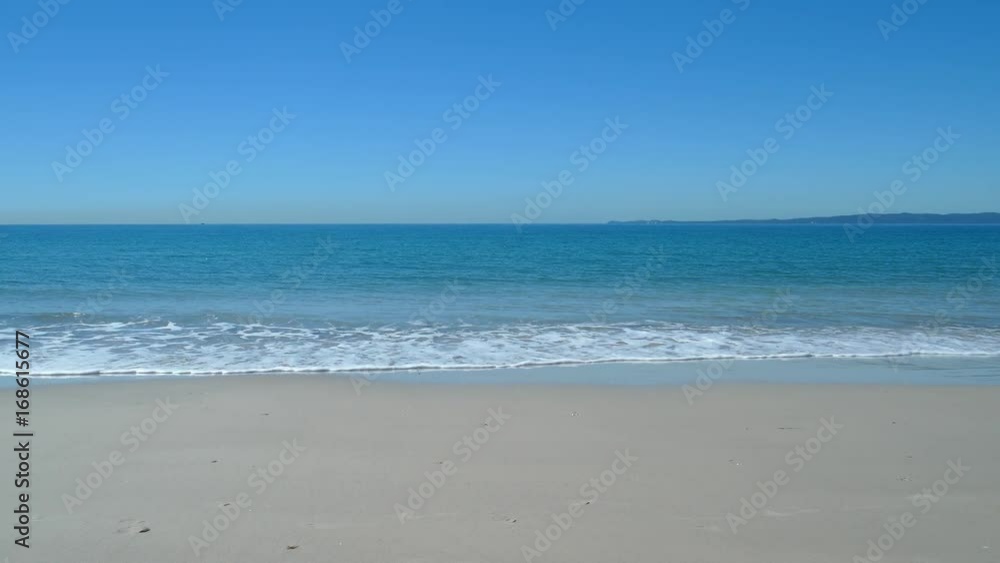 Wide shot of quiet beach with waves rolling in on a sunny day. Wide shot of quiet beach with waves rolling in on a sunny day.
