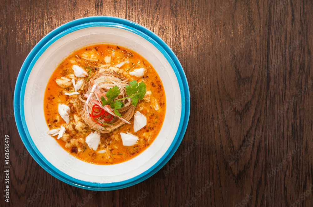 A bowl of Crab meat curry with vermicelli, Crab meat Laksa on wood table A bowl of Crab meat curry with vermicelli, Crab meat Laksa on wood table