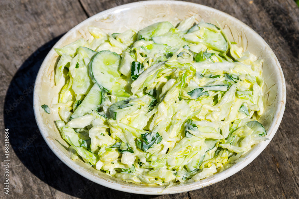 Spring salad with cabbage, cucumber, green onion, parsley and mayonnaise on wooden table