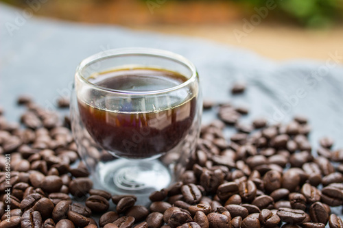 Black coffee in glass with bean coffee on black stone