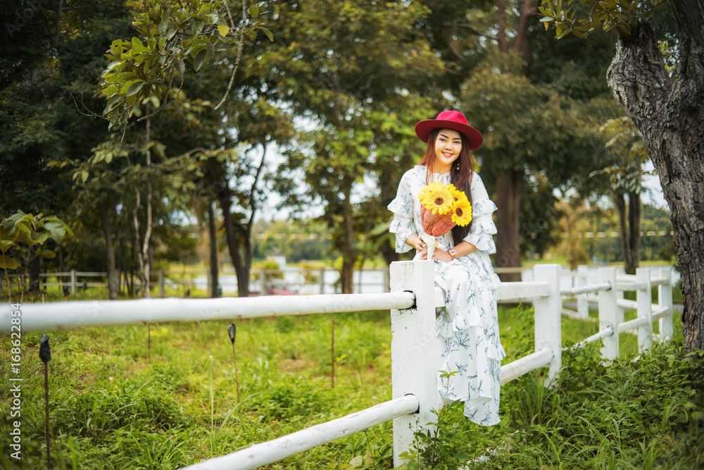 Young woman holding a yellow flower is on a white fence.
