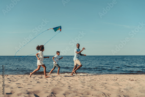 father and kids playing with kite on beach