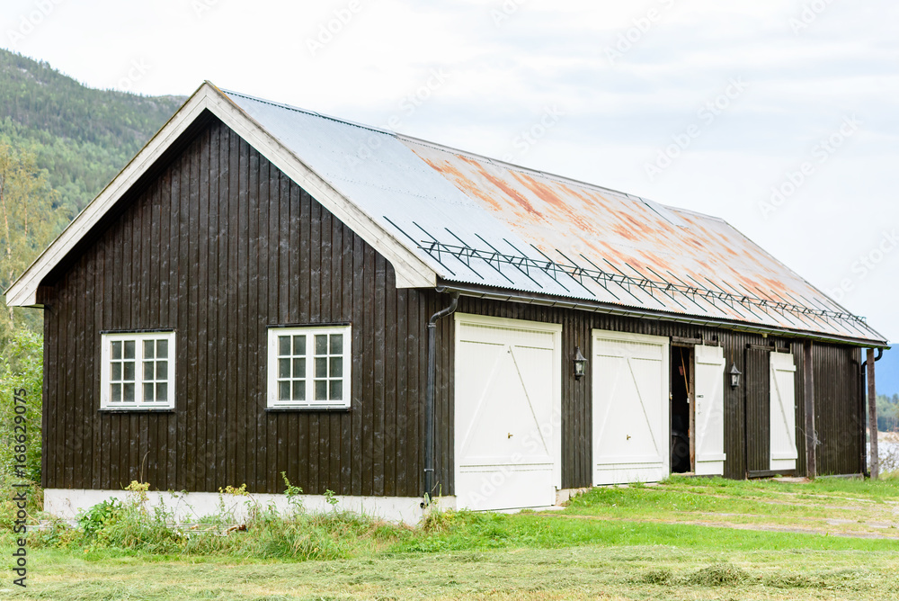 Black wooden garage and storage building with white doors. Snow railing on metal roof. Black wooden garage and storage building with white doors. Snow railing on metal roof.