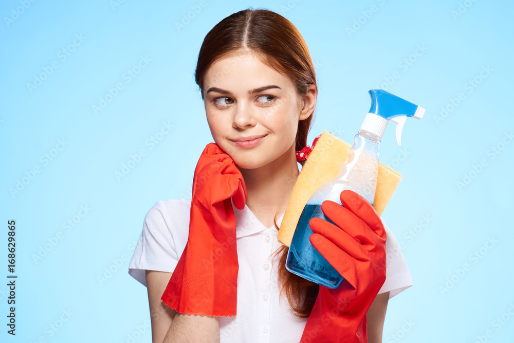 Beautiful young woman on a light blue background holds a detergent and a rag for cleaning the house, portrait Beautiful young woman on a light blue background holds a detergent and a rag for cleaning the house, portrait