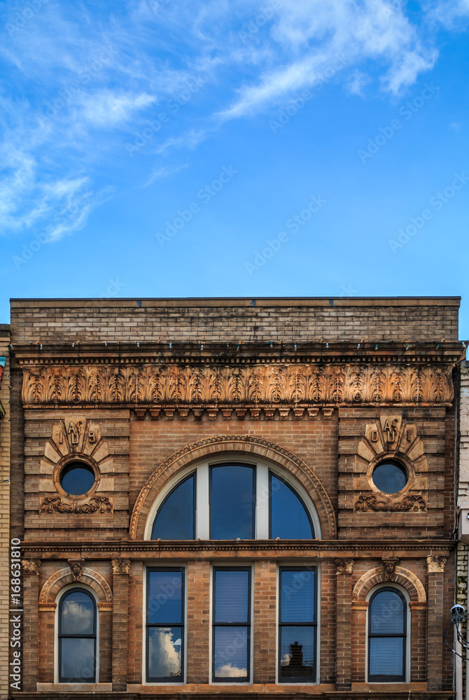 Upper facade of a building with old brick and curved windows It has circular windows. Clouds and blue sky are above the cornice.