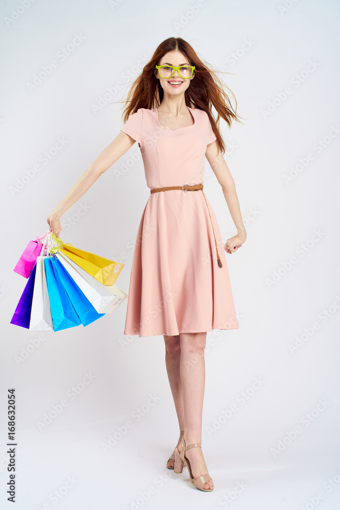 Beautiful young woman in glasses on a light background in full growth holds shopping Beautiful young woman in glasses on a light background in full growth holds shopping