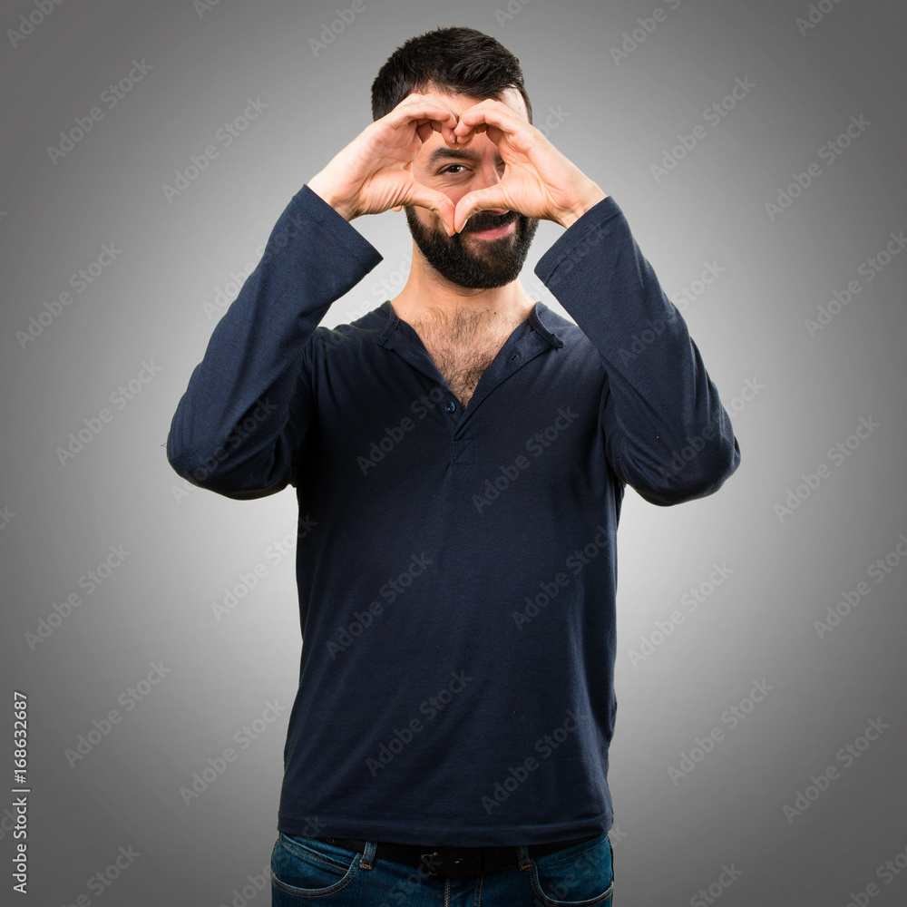 Handsome man with beard making a heart with his hands on grey background Handsome man with beard making a heart with his hands on grey background