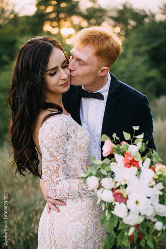 Happy newlyweds kissing at sunset, close-up, portrait photo