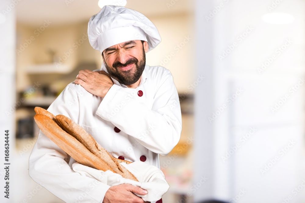 Young baker holding some bread with shoulder pain in the kitchen
