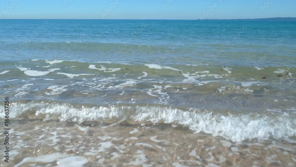 Wide shot of waves rolling in towards the beach on a sunny day.