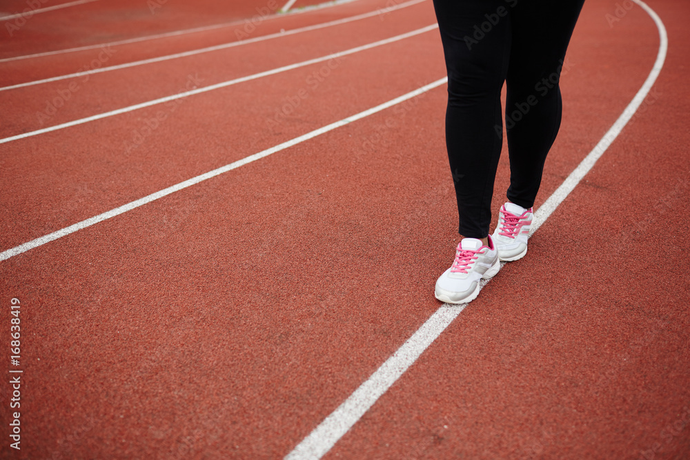 Legs of plus-sized woman walking down white line on stadium Legs of plus-sized woman walking down white line on stadium