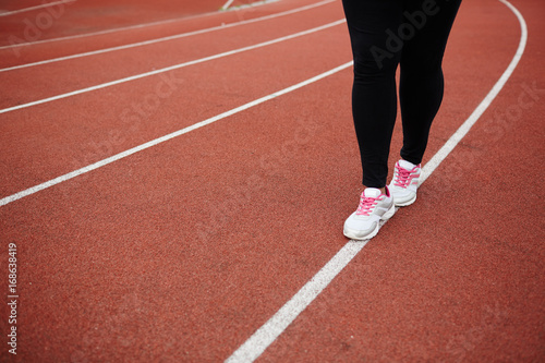 Legs of plus-sized woman walking down white line on stadium