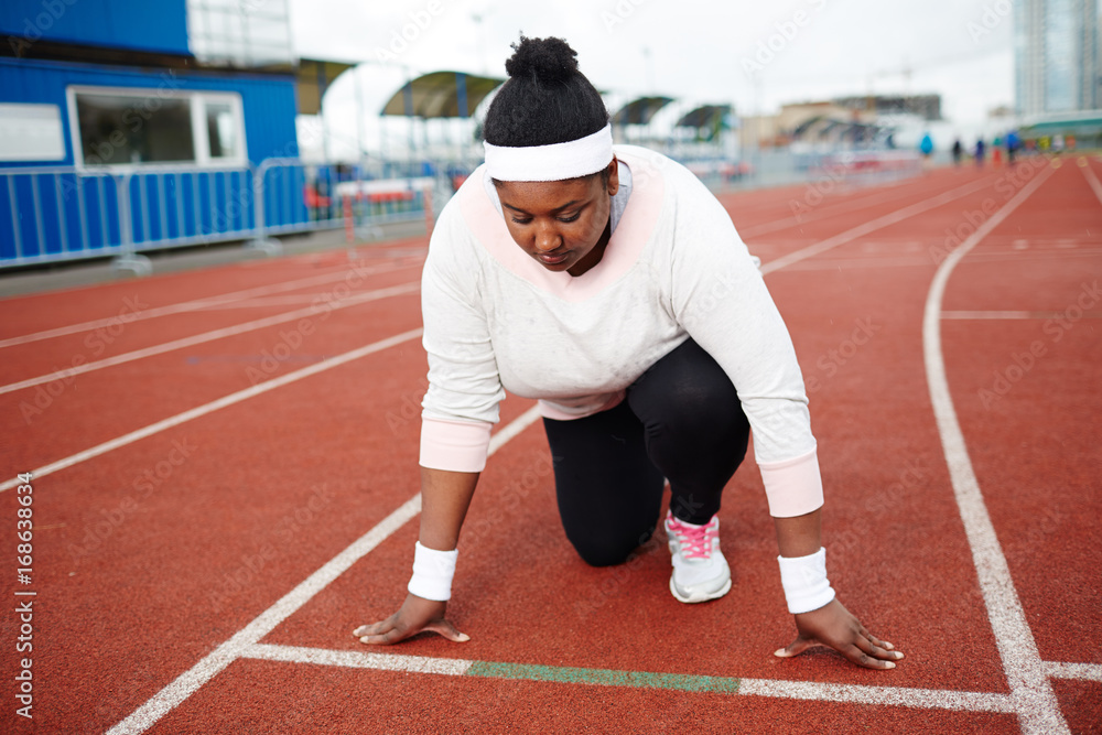 Young overweight woman standing by start line on racetrack ready to run