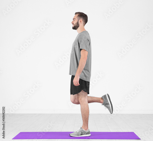 Schilderij op canvas Sporty young man training legs on mat in gym