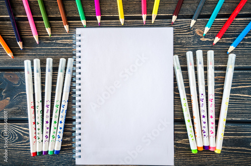 colored pencils, markers and Notepad on wooden background