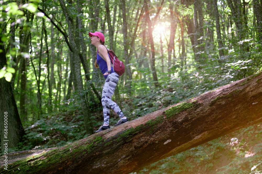 girl hiking in forest, climbing down the log with surprise expression on face
