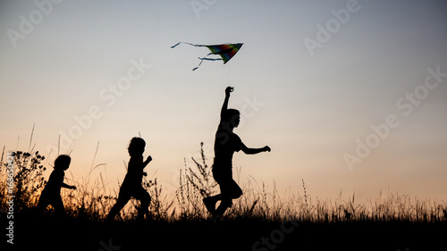 Children playing kite on summer sunset meadow silhouetted