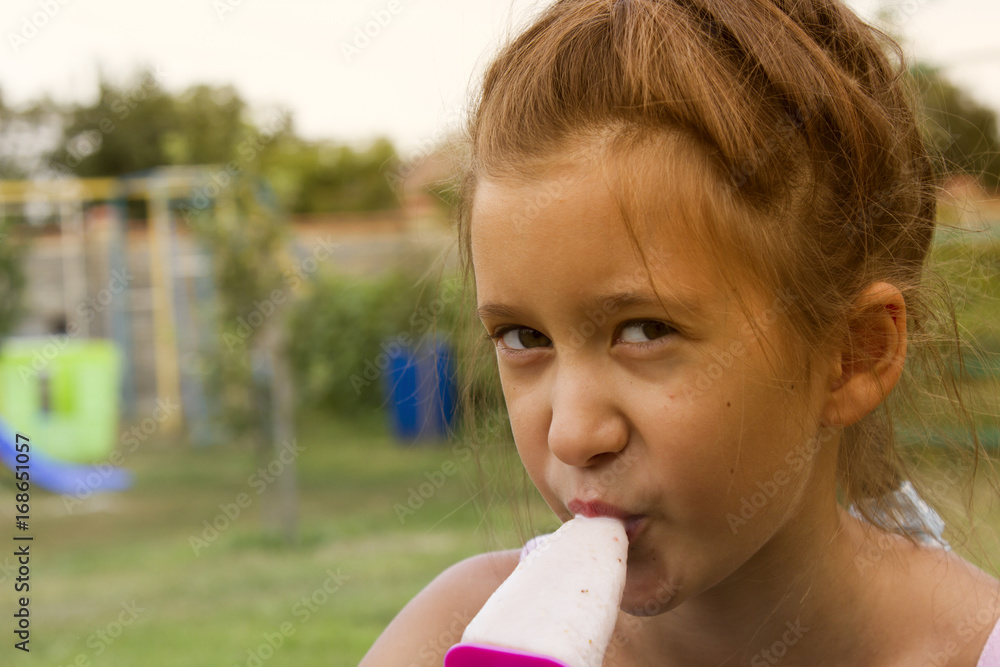 Beautiful child eating ice-cream outdoors in spring park against natural green background Beautiful child eating ice-cream outdoors in spring park against natural green background