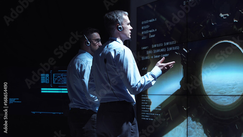 Back view of two supervisors standing at screen in space center and controlling landing on Moon.