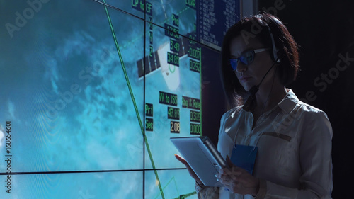 Side view of woman working at computer in space mission control center. Controlling the orbiting international space station ISS. Elements of this image furnished by NASA.