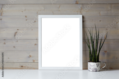Isolated interior shot of decorative fresh green plant in pot and blank photo frame with copy space for your picture, content or promotional information resting on white shelf at wooden wall. © shurkin_son