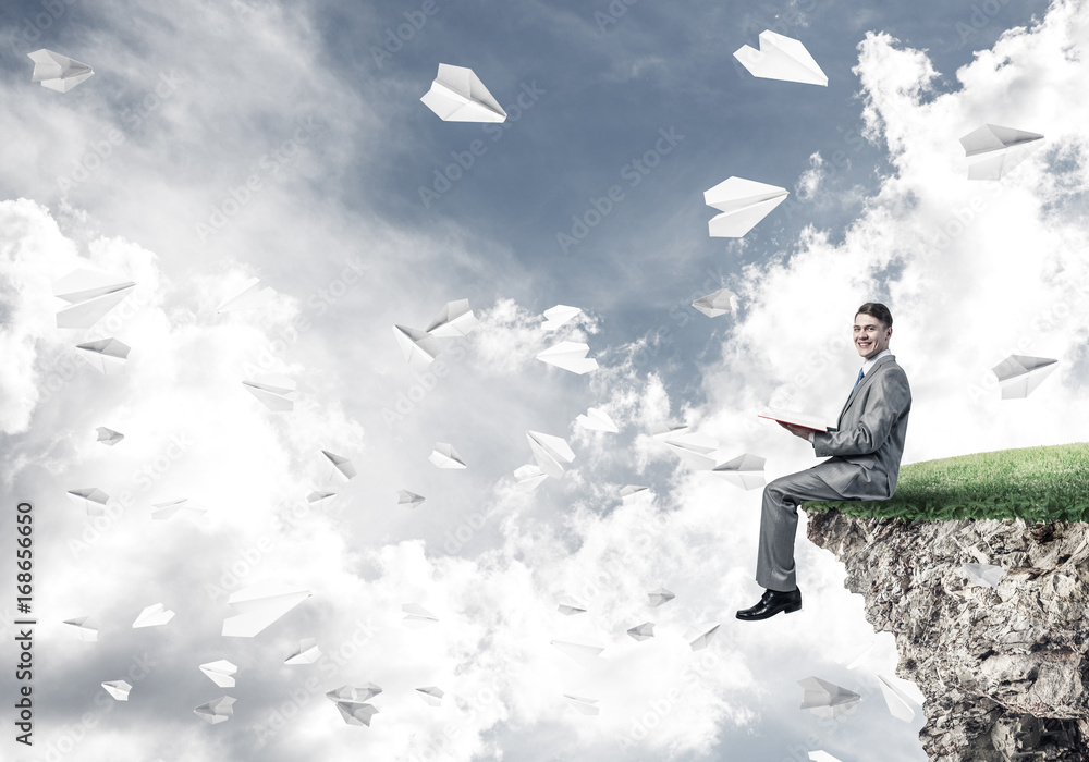 Man on edge reading book and paper planes flying in air Man on edge reading book and paper planes flying in air