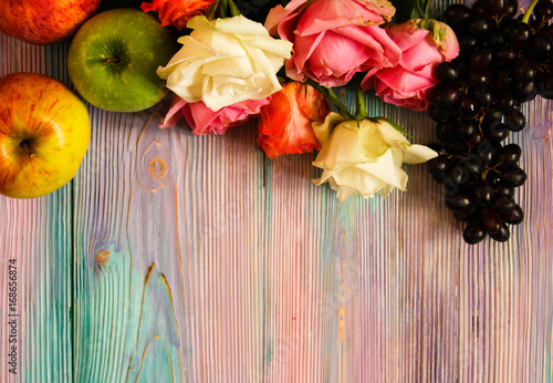 Colorful wooden background with roses, grapes and apples
