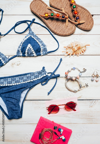 Flat lay of summer fashion with blue bikini swimsuit, and girl accessories on white wooden background