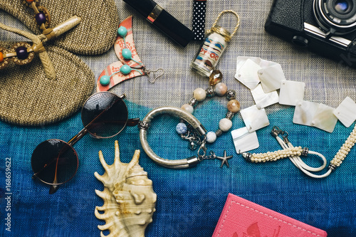 Flat lay of summer fashion with camera, slippers, sunglasses and other girl accessories on top of the bag as background