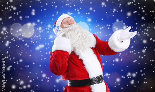 Santa Claus with headphones listening to Christmas music and snow effect on color background © Africa Studio