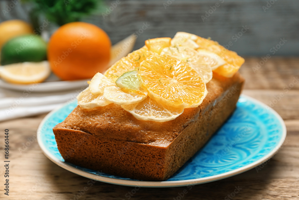 Plate with delicious citrus cake and sliced fruits on wooden table