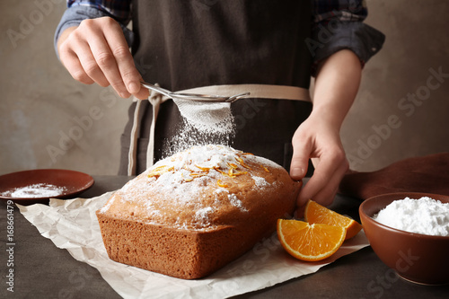 Woman covering delicious citrus cake with sugar powder