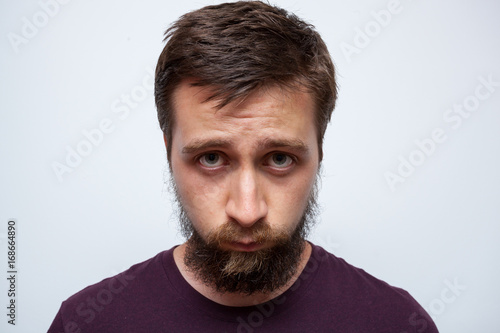 Young man looking at the mirror, disappointed or frustrated because of his messy beard