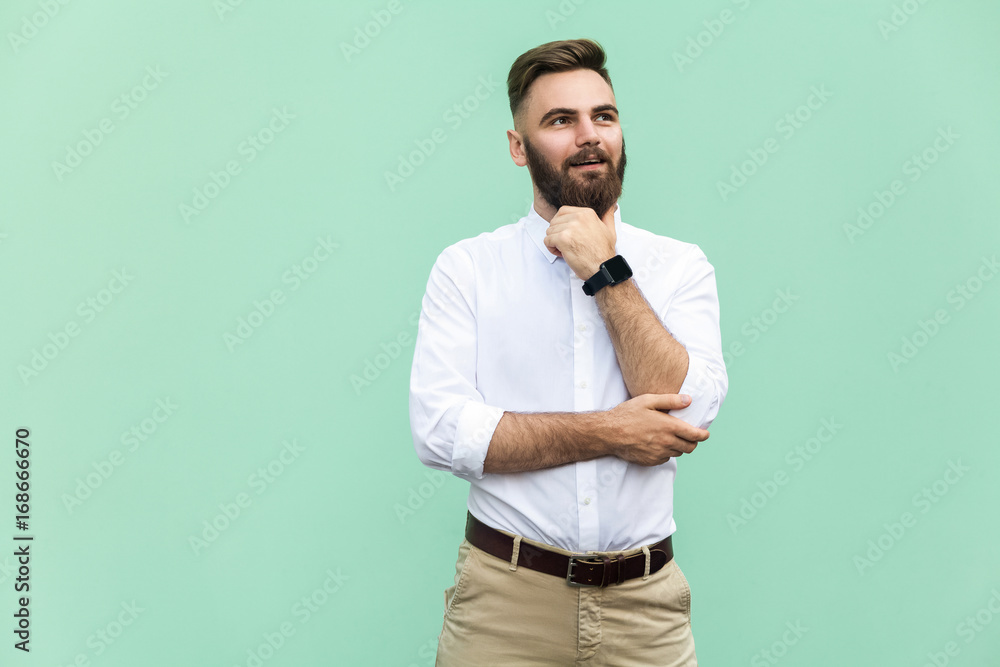 Thoughtful bearded businessman looking away while standing against light green wall. Studio shot - obrazy, fototapety, plakaty 