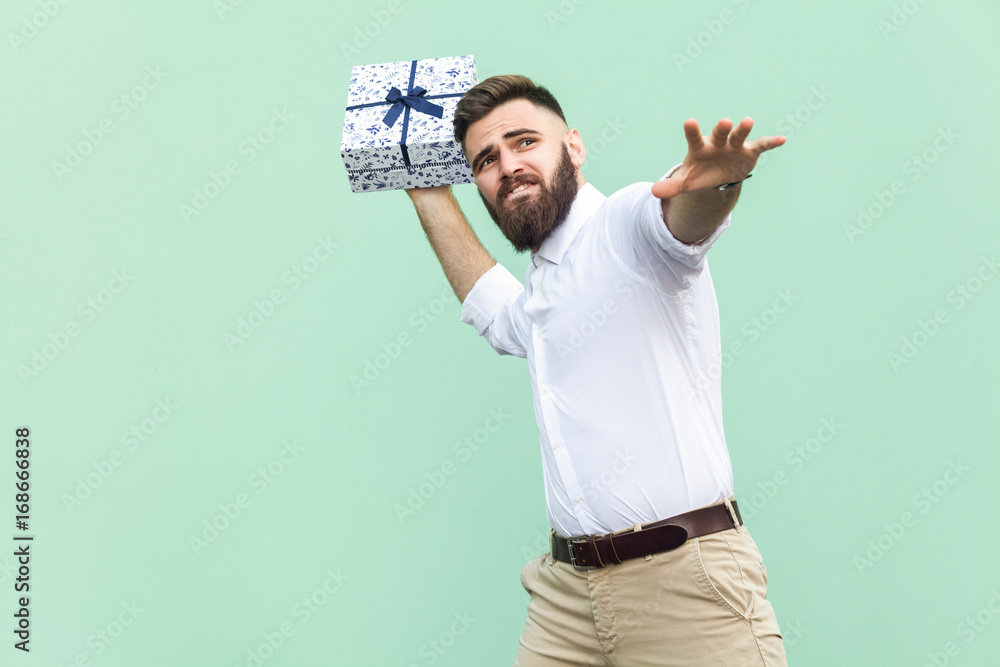 Φωτογραφία Catch your gift! Young adult man swung and wants to throw off your gift box, isolated on light green background