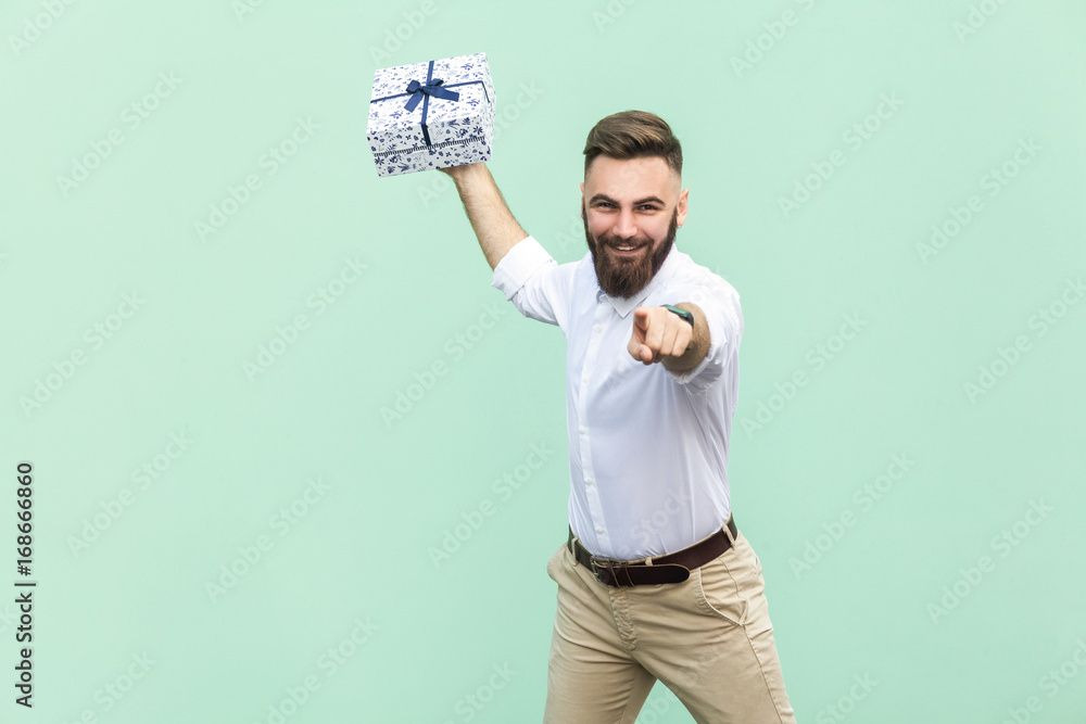 Φωτογραφία Its for you! Young adult businessman, holding gift box, pointing finger at camera and toothy smile