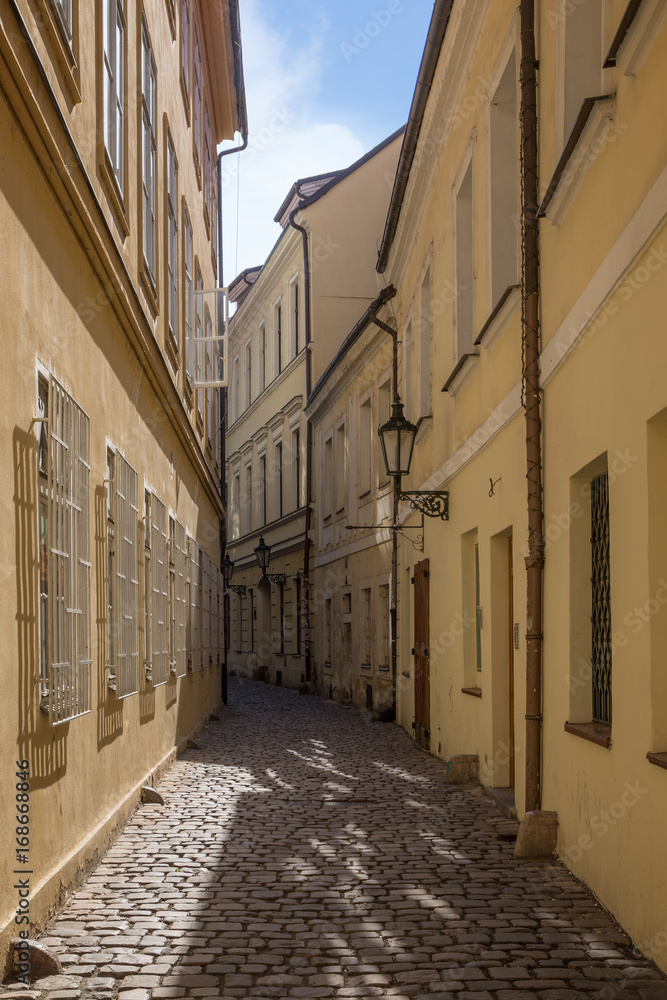 Narrow and empty cobblestone street and old buildings at the Old Town in Prague, Czech Republic on a sunny day.